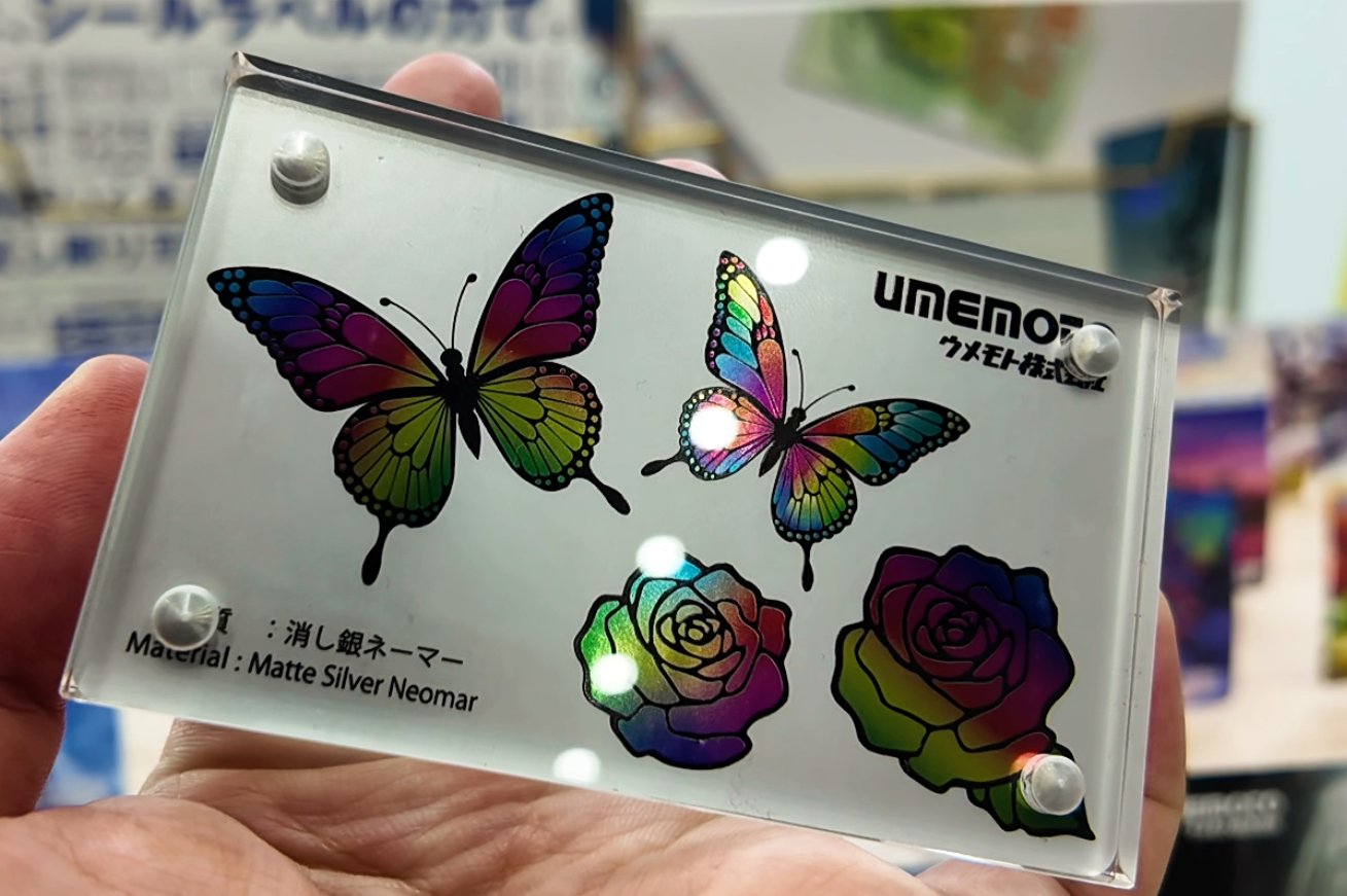 デジハク疑似箔シール実物サンプル — 消し銀ネーマー素材に蝶と薔薇を印刷。インクを載せた部分全体が光沢をもつ疑似箔表現。